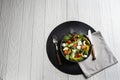 Black deep bowl with Greek salad, knife and fork on a black round stand. Royalty Free Stock Photo