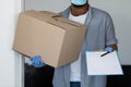 Black delivery man wearing mask and gloves, holding cardboard box and clipboard