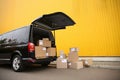 Black delivery van and many different parcels near yellow building outdoors. Courier service