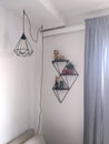 Black designer geometric lamp hanging on a cord with shelves on a wall and curtains
