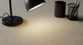 Black desk lamp with a round base illuminates a textured beige surface. Next to it, a Royalty Free Stock Photo