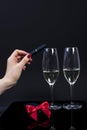 Black device in a female hand with red manicure and 2 glasses with champagne on a black background,