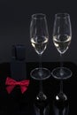 Black device with a red bow and 2 glasses with champagne on a black background