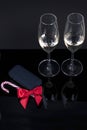 Black device with a red bow and two glasses with champagne on a black background, and a Christmas candy.