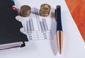 Black diary, a pen and a stack of coins on financial charts Royalty Free Stock Photo