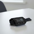 A black digital wrist device sits on a white table. The screen displays an EKG waveform, Royalty Free Stock Photo