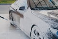 Black dirty car in white soap foam at car wash service station Royalty Free Stock Photo