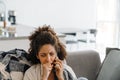 Black displeased woman talking on mobile phone while sitting on sofa Royalty Free Stock Photo