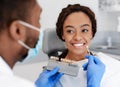 Black doctor holding tooth scale sample over smiling young woman Royalty Free Stock Photo