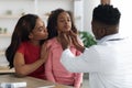 Black doctor palpating school girl throat at clinic