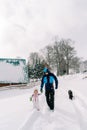 Black dog follows a dad walking hand in hand with a little girl along a snowy road in the village Royalty Free Stock Photo