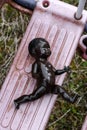 Black doll lying on dirty swing at abandoned playground