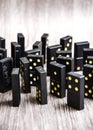Black dominoes on a light wooden table stand in a row, selective focus