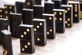 Black dominoes on a light wooden table stand in a row, selective focus