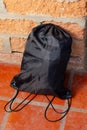 Black drawstring backpack resting on red tile floor beside brick wall Royalty Free Stock Photo