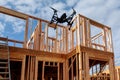 Black drone quadcopter with camera flying over residential construction home framing against Royalty Free Stock Photo
