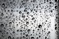 Black drops of water with a white glow on the glass against a blurred cloudy sky background on a rainy day. Selective focus Royalty Free Stock Photo