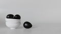 Black eggs fall from a white ceramic cup on a gray background.