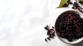 Black elderberry berries in bowl on white marble background. Top view, copy space.