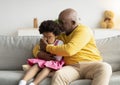 Black elderly man calming upset sad crying little girl in living room interior