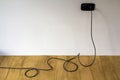 Black electric cable in wall socket on wooden parquet floor Royalty Free Stock Photo