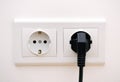 Black electric chord plugged into a white electricity socket on white background