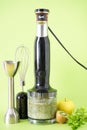Black electric hand blender and accessories with fruits and smoothie ready on green background, vertically Royalty Free Stock Photo