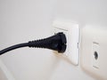 Black electric power plug on white socket on white wall
