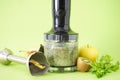 Black electrical hand blender and accessories with fruit on a green background, close up