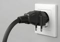 Black electrical plug being inserted into a white wall socket Royalty Free Stock Photo