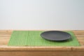 Black empty plate and bamboo placemat on wooden table. Chinese kitchen or restautant concept background
