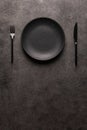 black empty plate and cutlery, fork and knife on a dark textured background. The concept of a layout for the design of a Royalty Free Stock Photo