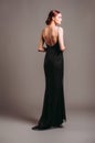 Black evening dress. Elegant lady in full-length backless sleeveless vintage gown with straps. Studio portrait of a beautiful youn Royalty Free Stock Photo