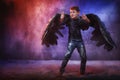 Black evil angel on a dark background with colored lighting. The concept of war between good and evil. Boy with angel wings during