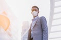 black executive man wearing suit, mask, standing outside building in city with sunrise or sunset. Royalty Free Stock Photo