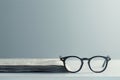 Black eyeglasses lie on a stack of folded newspaper. Generative AI Royalty Free Stock Photo