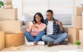 Black family chatting online with friends, showing key to new house on camera, sitting among carton boxes on moving day Royalty Free Stock Photo