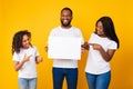 Black family holding blank white advertising billboard at yellow studio Royalty Free Stock Photo