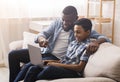 Black father and little son using laptop at home, surfing internet