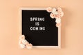Black letter board with Spring Is Coming white text and flowers. Blooming floral wooden frame. Waiting for spring concept