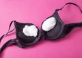 Black female bra with cotton wool inside on a pink background. The concept of augmentation of the female breast with plastic Royalty Free Stock Photo