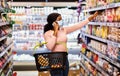 Black female consumer in mask making call on cellphone while shopping for groceries, taking product from shelf at mall Royalty Free Stock Photo