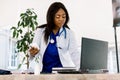 Black female doctor at work in an office, looking to laptop. Beautiful African American woman doctor or nurse working on Royalty Free Stock Photo