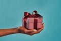 Black female hand holding gift box on blue Royalty Free Stock Photo