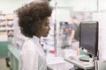 Black female pharmacist at pharmacy. Close up side view of pretty woman pharmacist working with computer behind counter Royalty Free Stock Photo