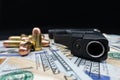 Black firearm and bullets close-up on a pile of United States currency against a black background.