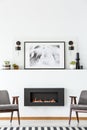 Black fireplace between grey armchairs in white flat interior wi