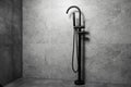 Black floor standing bath taps, on the background of dark grey bathroom walls. Royalty Free Stock Photo