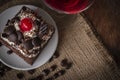 Black Forest Cake topping cherry putting on the white plate on the sack and wood background there are coffee bean and glass placed Royalty Free Stock Photo