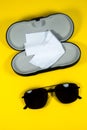 Black frame mens sunglasses with glasses cleaning cloth and case on a yellow background